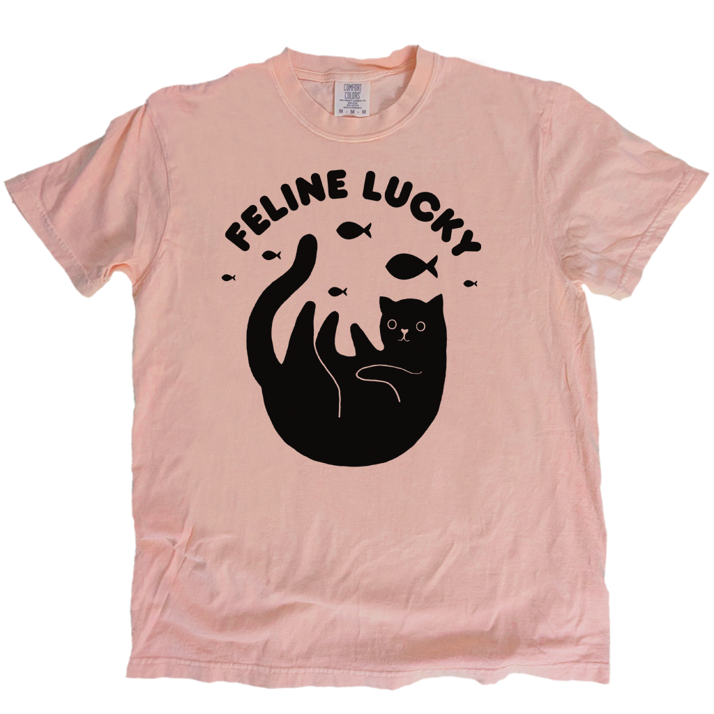 Pink t-shirt with black cat graphic and 'Feline Lucky' text on a white background