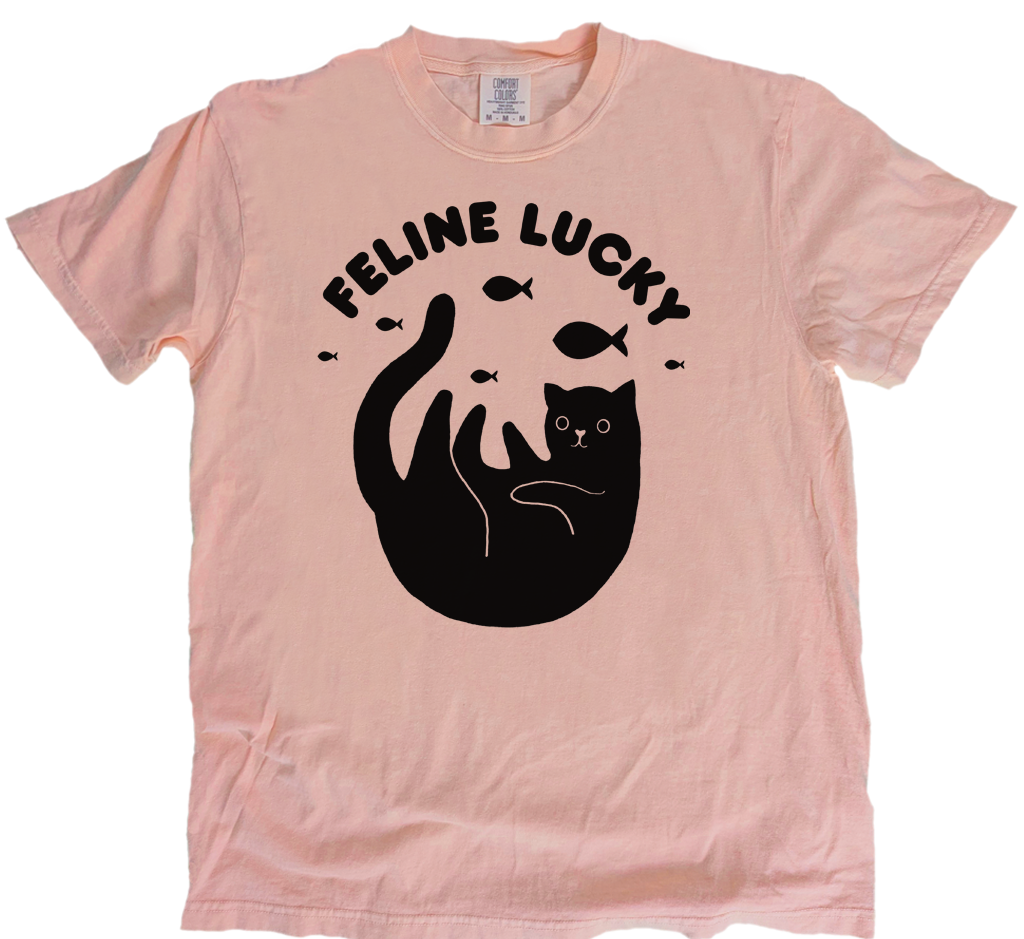 Pink t-shirt with black cat graphic and 'Feline Lucky' text on a white background